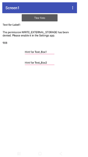 A mobile app screen titled "Screen1" showing a button labeled "Tirar foto," a message about denied WRITE_EXTERNAL_STORAGE permission, a number "908," and two input boxes with hints "Hint for Text_Box1" and "Hint for Text_Box2." (Captioned by AI)